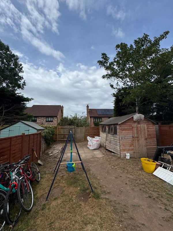 Back garden cleared to bare ground beside sheds, bicycles and a swing frame