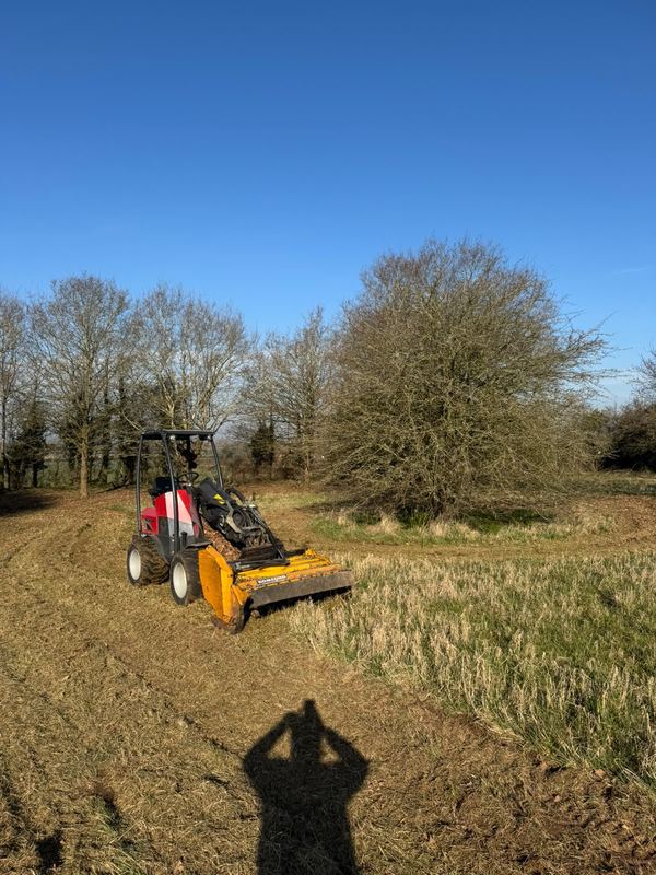Tracked flail mower clearing rough grass and scrub on open ground