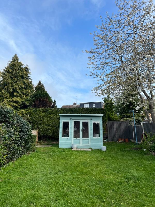 Neat lawn and planted borders around a pale green summerhouse